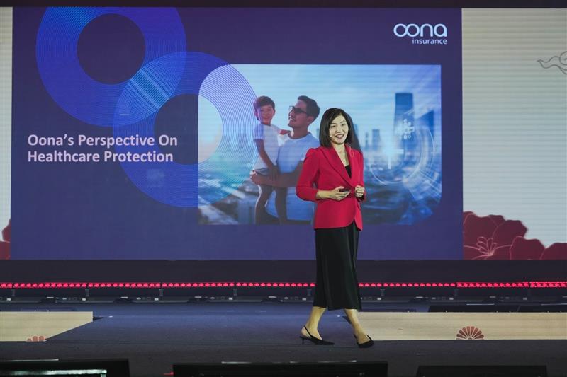 Mylene Ong, Oona’s Group Chief Marketing Officer presenting “Oona’s Perspective on Healthcare Protection” on stage during a financial event, with a large Oona Insurance presentation slide in the background.