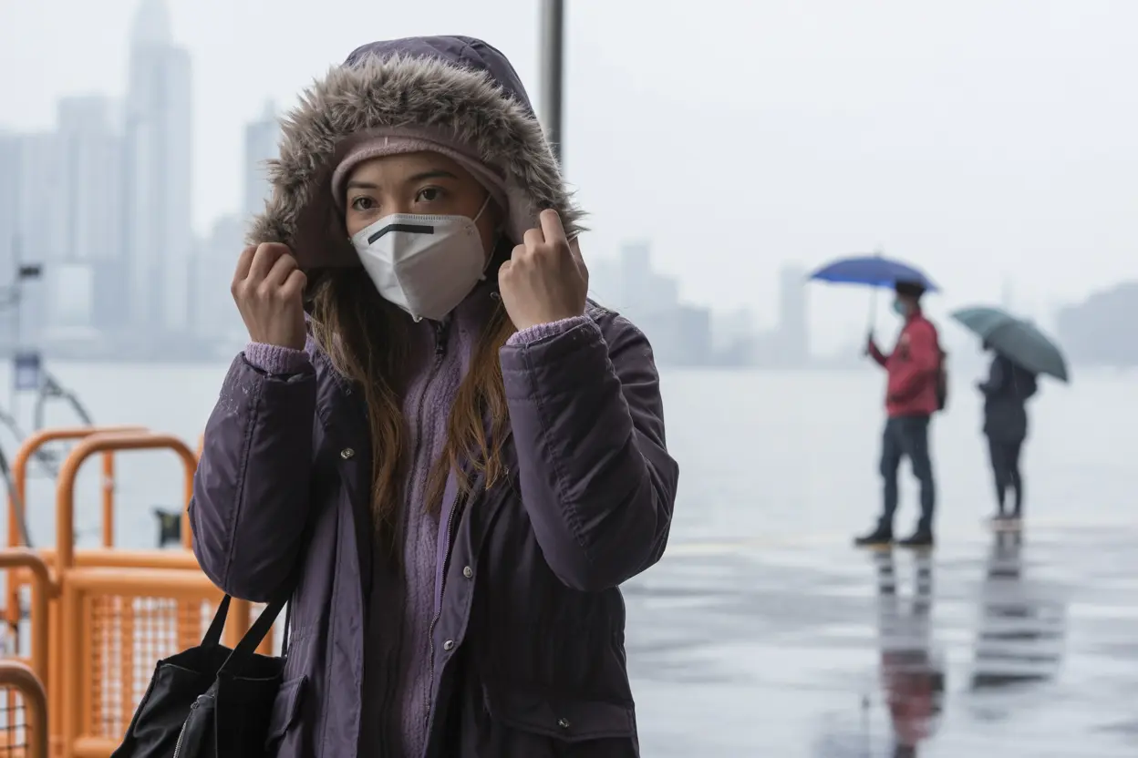 A young Filipina wearing a purple winter coat with a fur-trimmed hood and a white N95 face mask.
