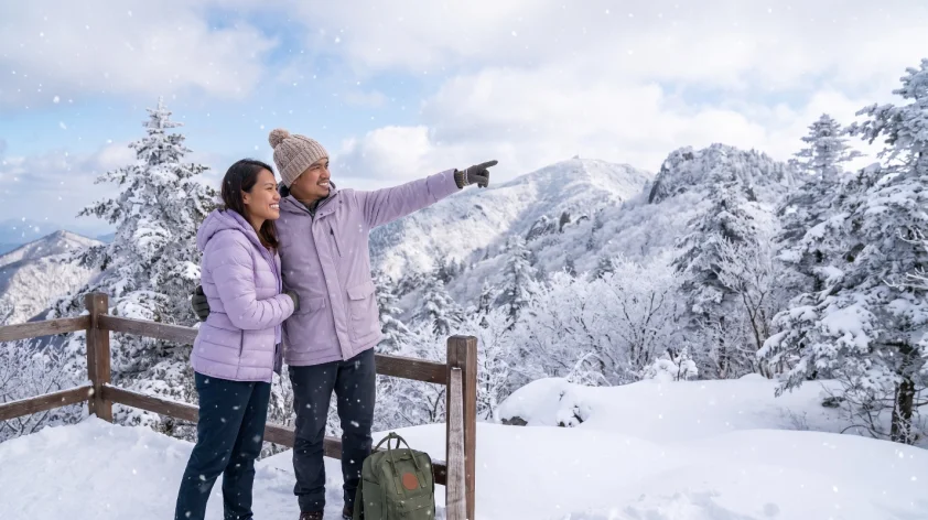 A couple Filipino traveler in a light purple winter jacket enjoying a snowy winter escape in Asia, surrounded by snow-covered mountains.